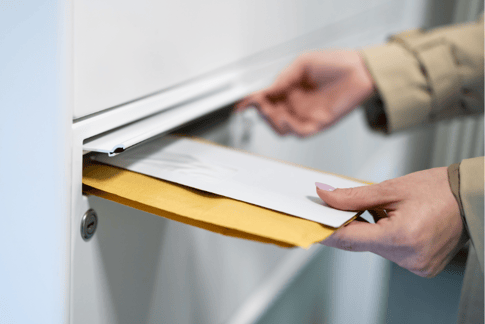 Eine Hand wirft einen Briefumschlag in einen Briefkasten