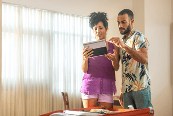 Paar schaut auf Tablet, vor ihnen ein geöffneter Koffer